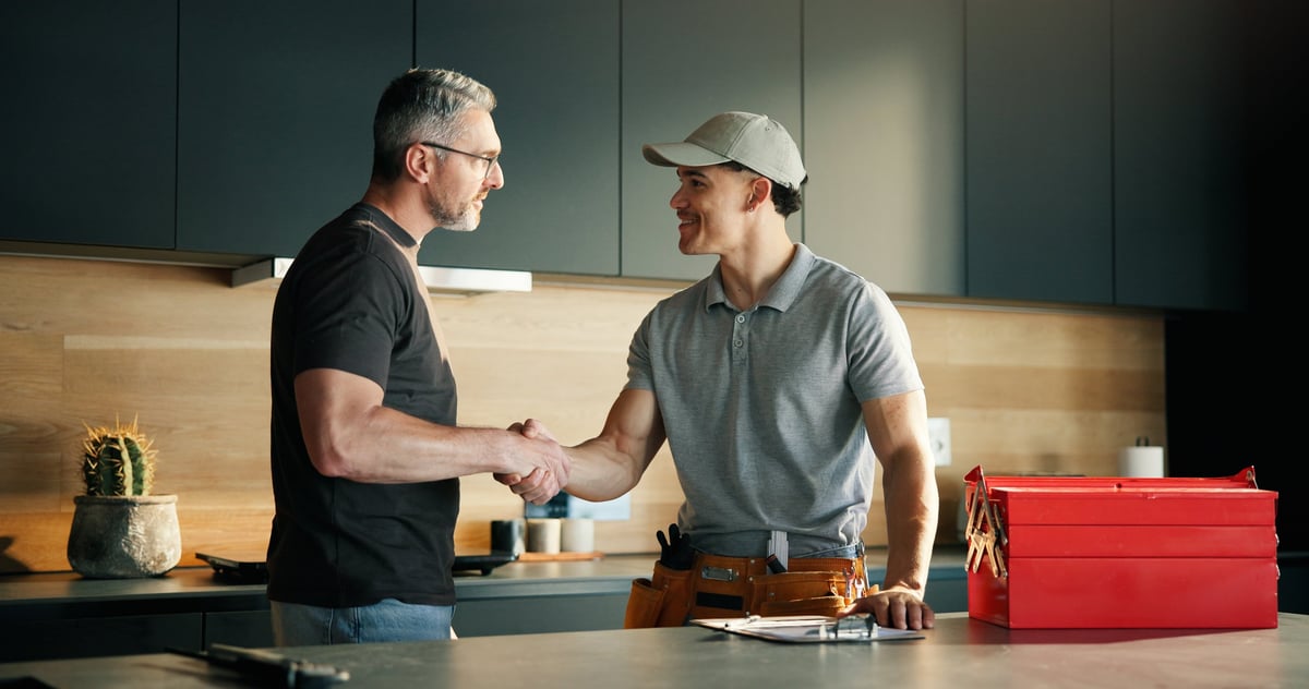 Professional plumber shaking hands with homeowner in kitchen after completing service